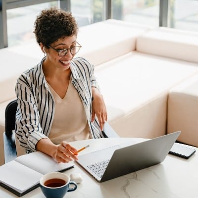 Smiling student learning online with coffee and notebook, symbolising the accessibility of the accredited Sleep Well Coach Training self-study programme.